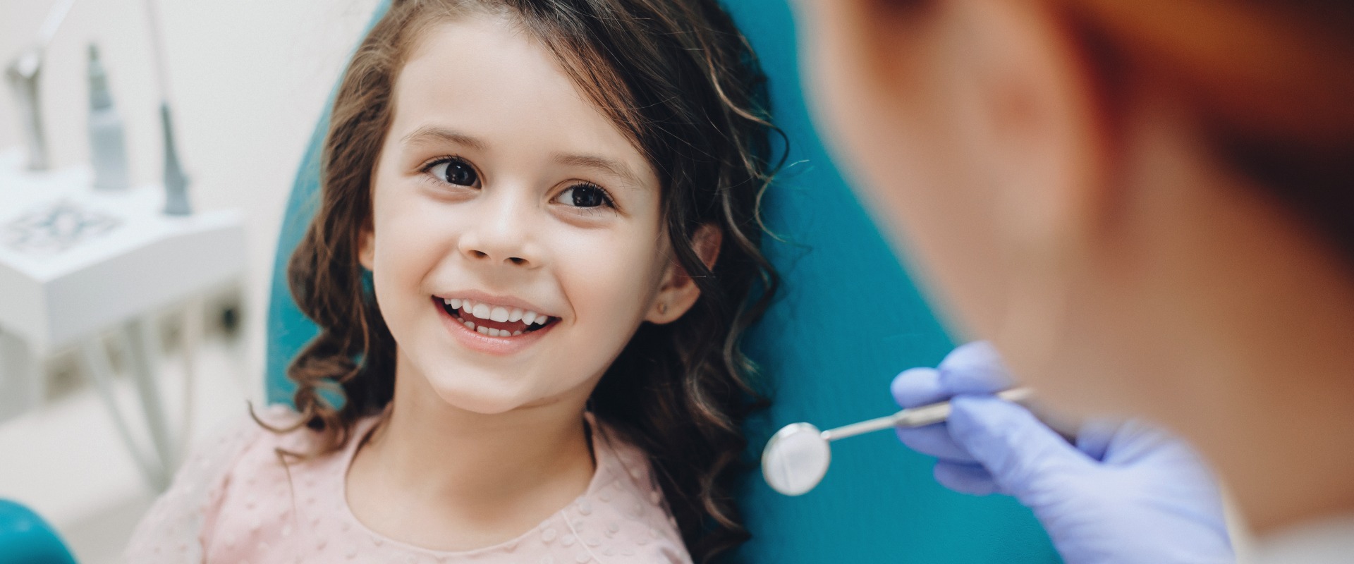 Curly haired little girl looking and smiling to the dentist after a checking up jpg