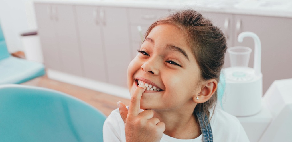 Mixed race little patient showing her perfect toothy smile while sitting dentists chair jpg