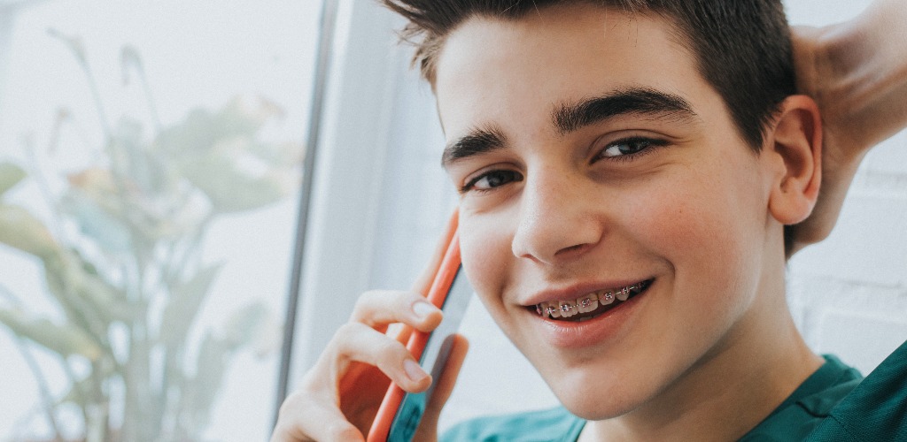 Portrait of a male teenager with braces and mobile phone jpg