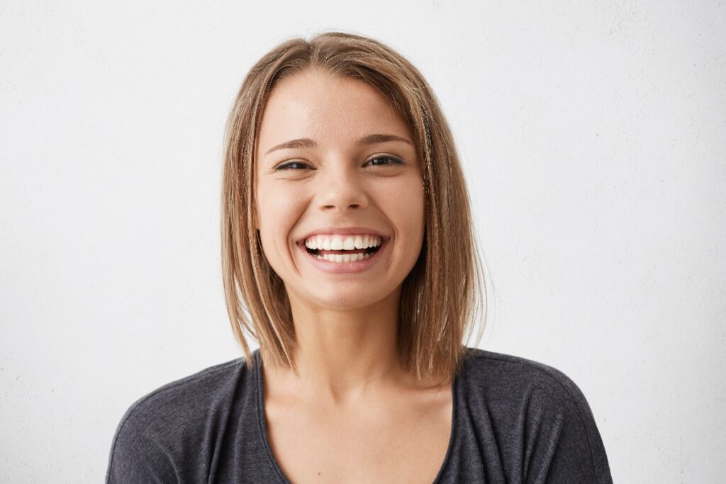 Positive human facial expressions and emotions cheerful attractive teenage girl with bob hairstyle grinning broadly showing her perfect white teeth at camera while spending nice time indoors jpg