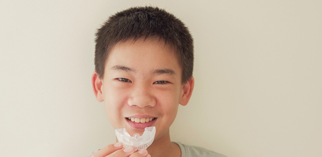 Smiling asian preteen boy holding invisalign braces mouthguard teen orthodontic oral health care concept jpg