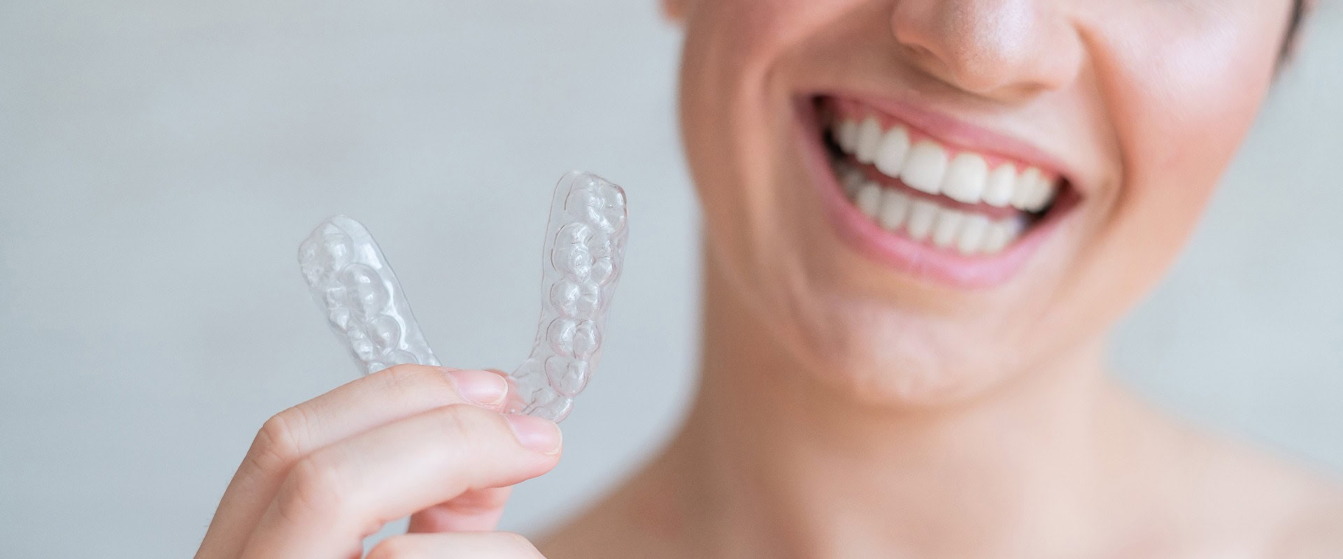 Nahaufnahme einer kieferorthopädischen transparenten Silikonzahnspange in weiblichen Händen. Eine Frau mit einem perfekten, charmanten Lächeln hält eine herausnehmbare Nachtspange. Zahnspange für die Zahnaufhellung. Ausgeschnittenes Foto.