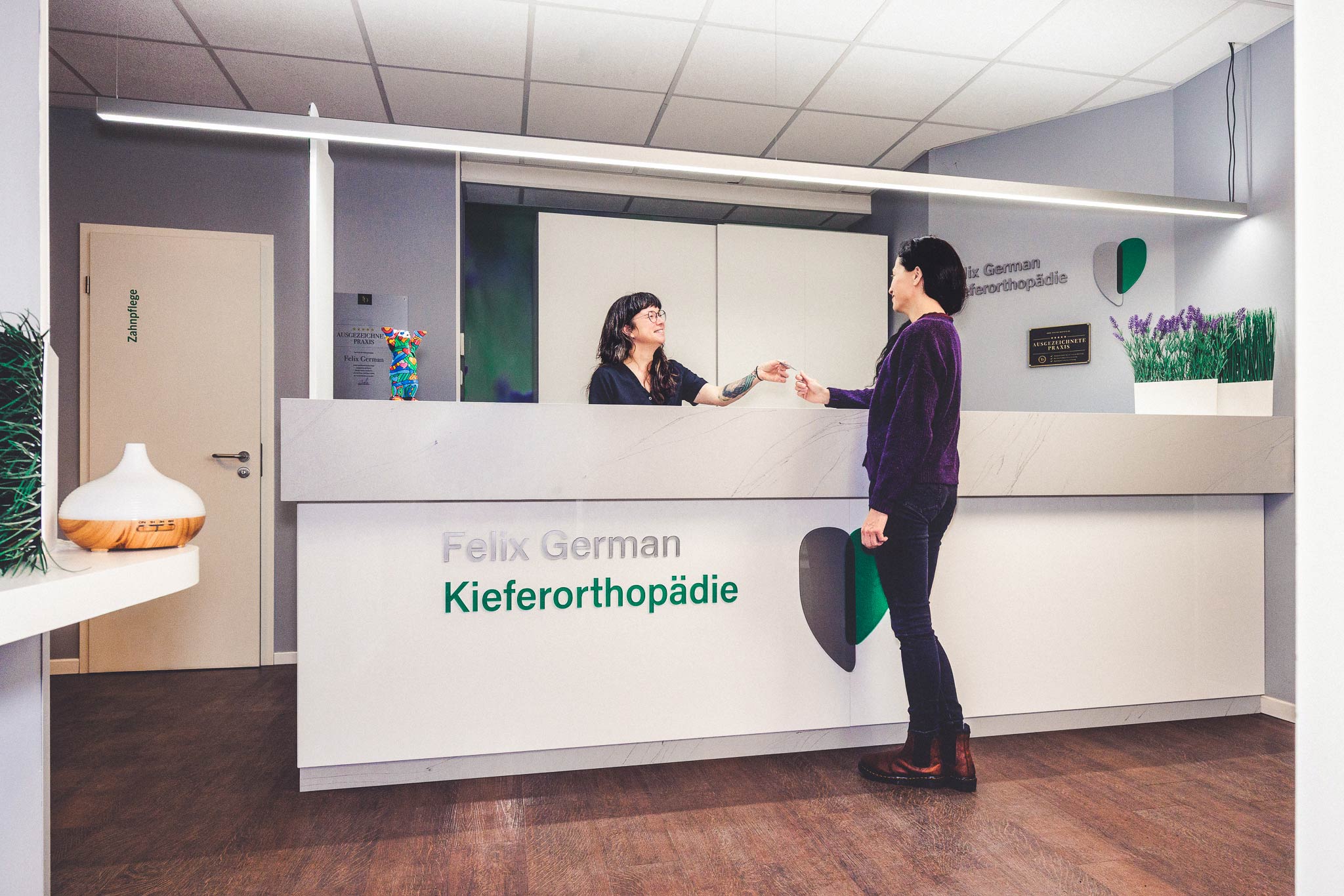 Zwei Personen in einer hellen Zahnarztpraxis, eine überreicht der anderen ein Dokument